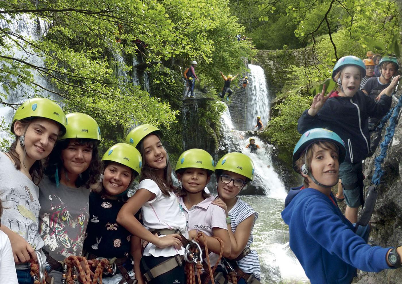 grupo de niños con cascos delante de una cascada